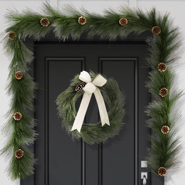 a christmas wreath with pine cones and white ribbon hanging on a black front door,