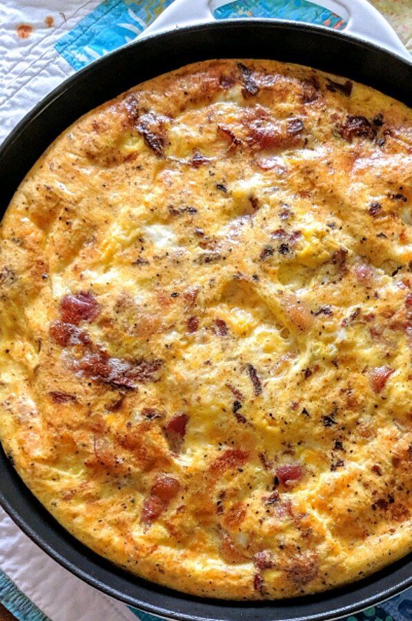 an omelet with bacon and cheese in a black pan on a blue table cloth