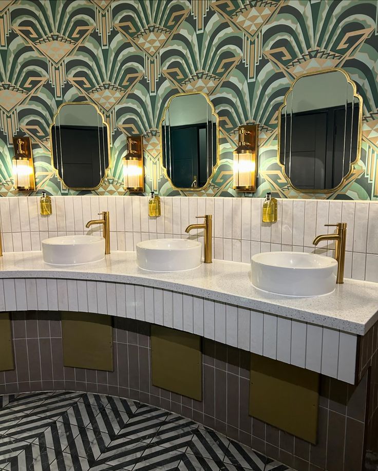 a bathroom with two sinks and three mirrors on the wall above them are gold faucets