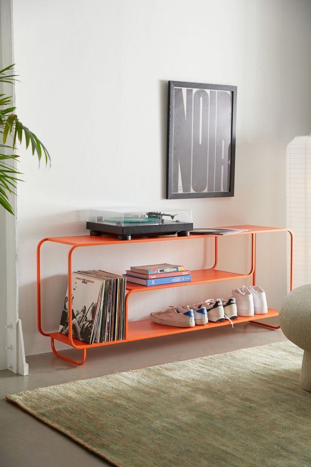 an orange shelf with records and magazines on it in front of a wall mounted television