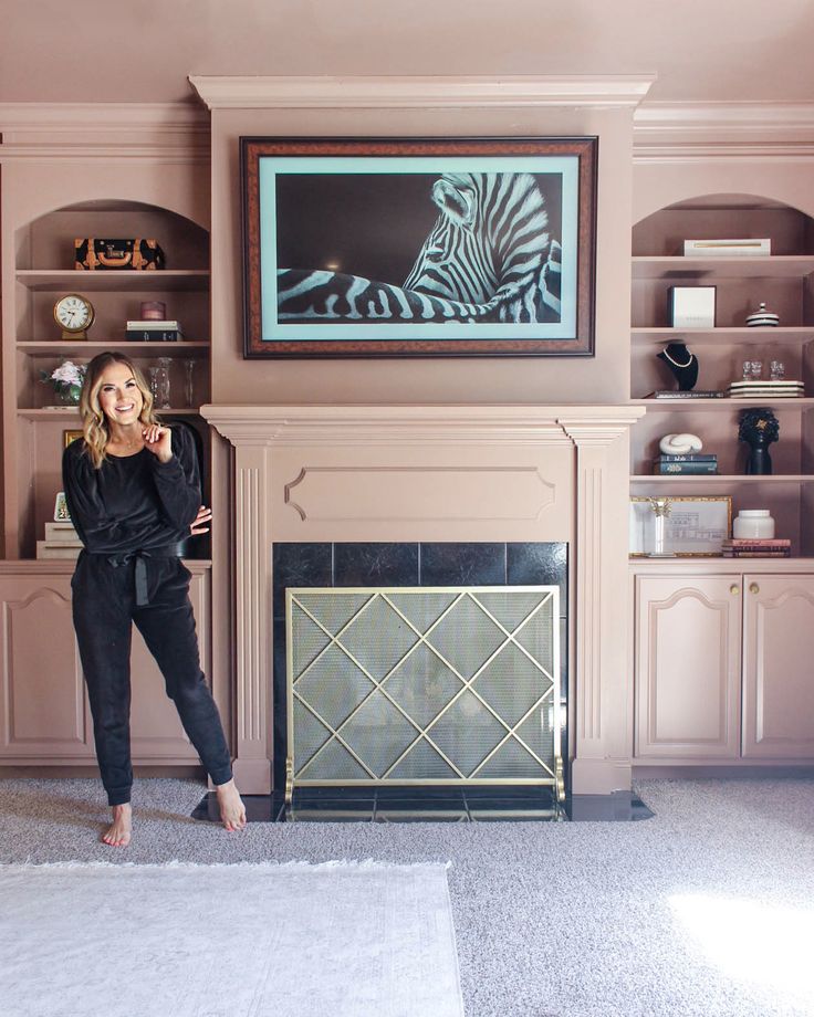 a woman standing in front of a fireplace with a zebra painting on the wall behind her