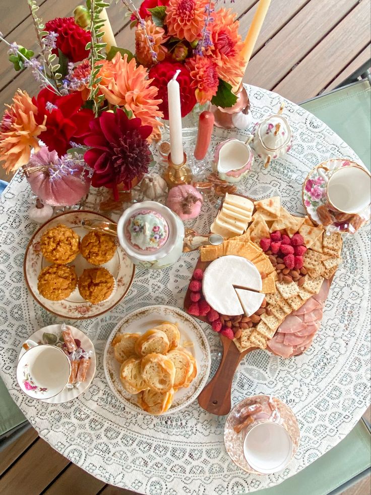 a table topped with plates and bowls filled with food next to flowers on top of a wooden floor