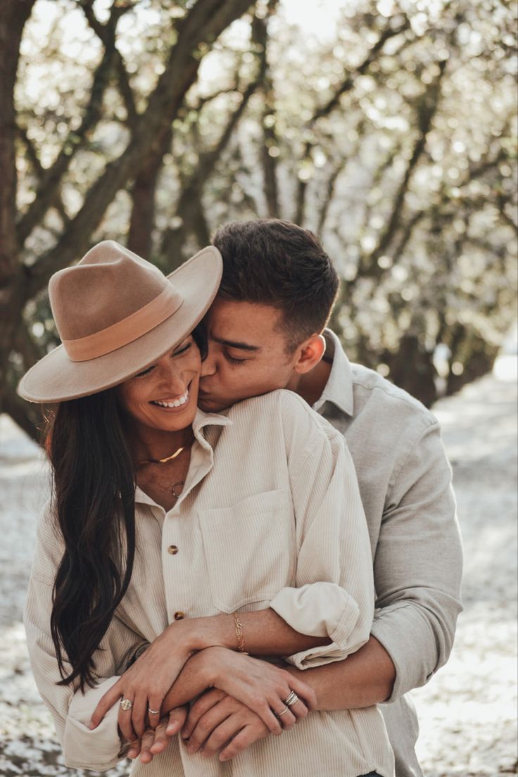 a man and woman hugging each other in front of trees