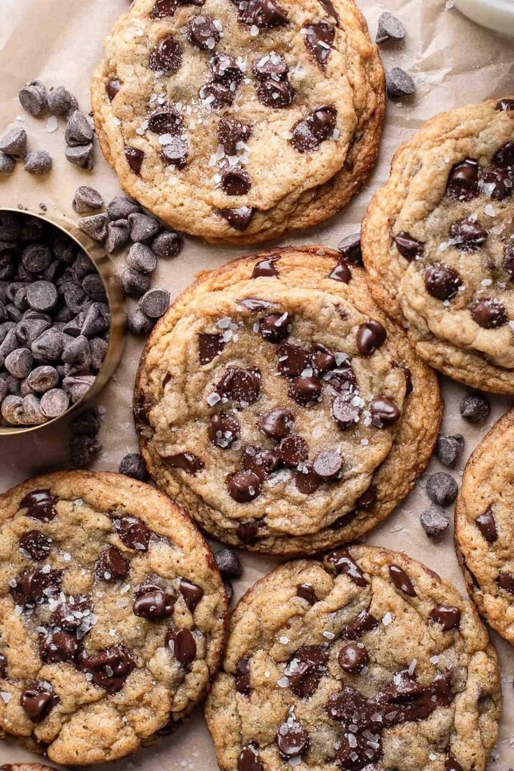 chocolate chip cookies are arranged on top of parchment paper and next to a measuring cup