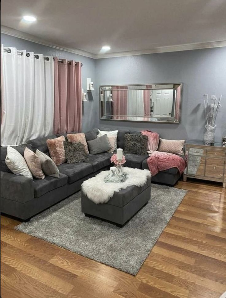 a living room with grey couches and pink curtains