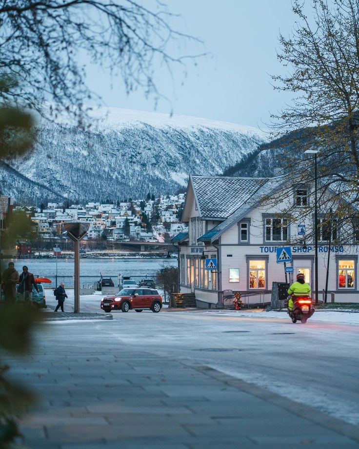 a man riding a motorcycle down a street next to a snow covered mountain side town