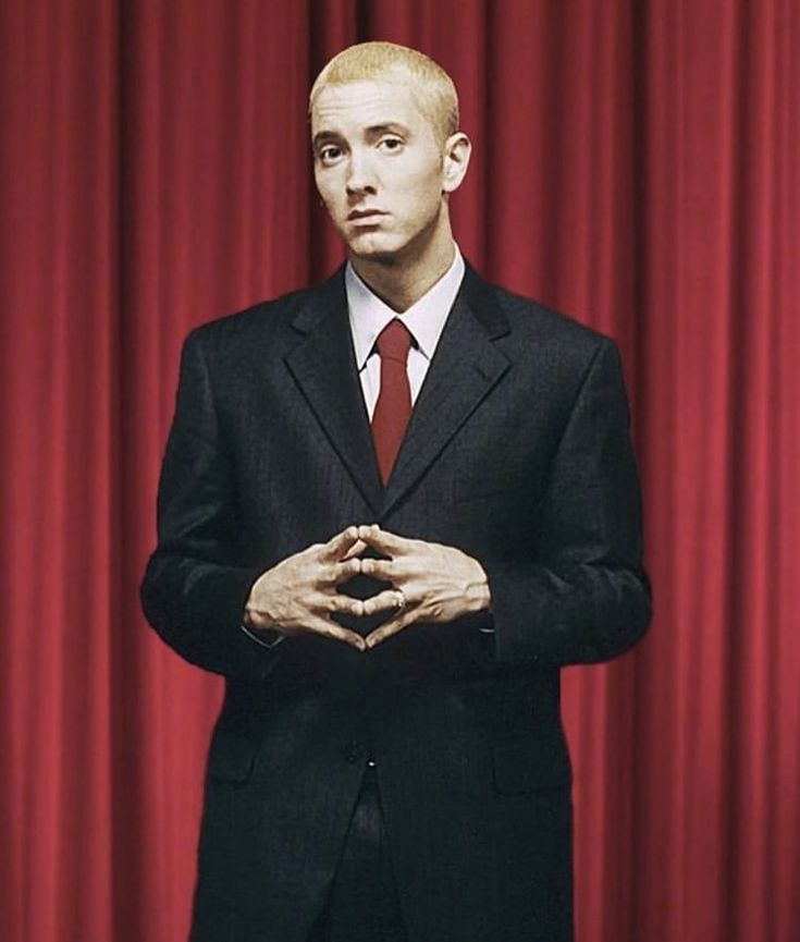 a man standing in front of a red curtain with his hands folded up to the chest