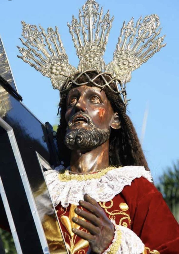 a statue of jesus wearing a crown and holding a cross in front of a blue sky