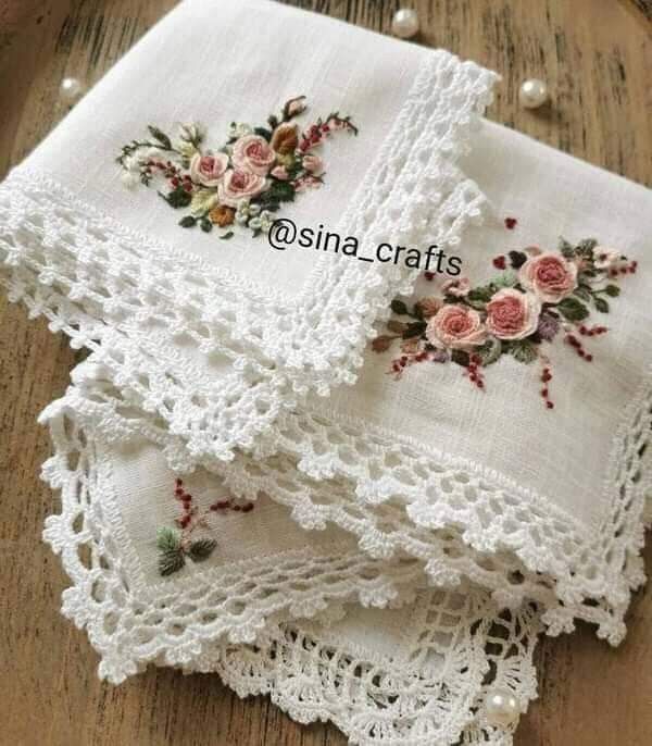 three embroidered napkins with flowers on them sitting on a wooden table next to pearls