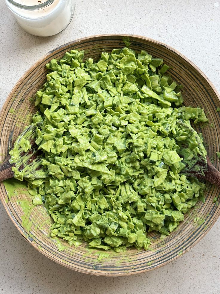 a bowl filled with green food next to a cup