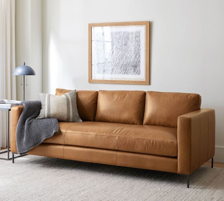 a living room with a brown leather couch and white rugs on the floor next to a window