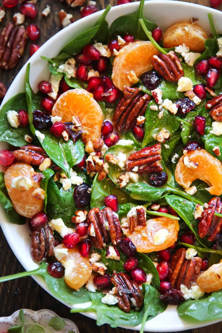 a white bowl filled with spinach salad topped with oranges and pecans