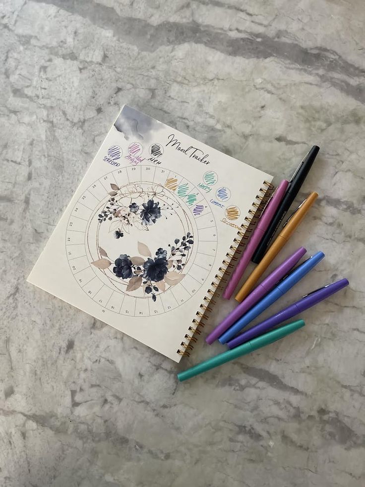 four colored pencils are next to a spiral notebook with the zodiac sign on it