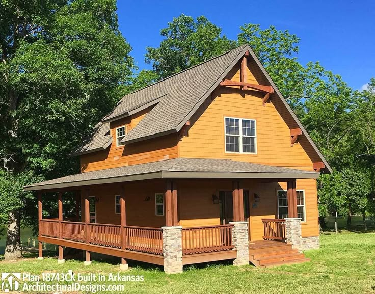 a large wooden house sitting on top of a lush green field in front of trees