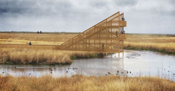 a wooden structure sitting on top of a lush green field next to a lake and tall dry grass