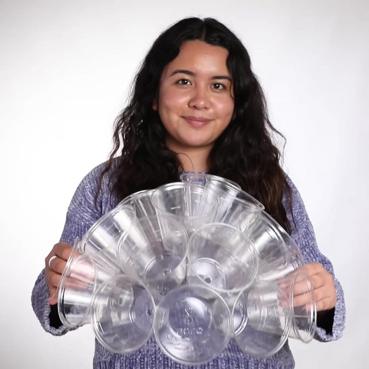 a woman holding a large stack of clear plastic plates in front of her face and smiling at the camera