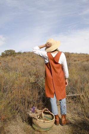 a woman in an orange vest and straw hat standing on a field with a basket