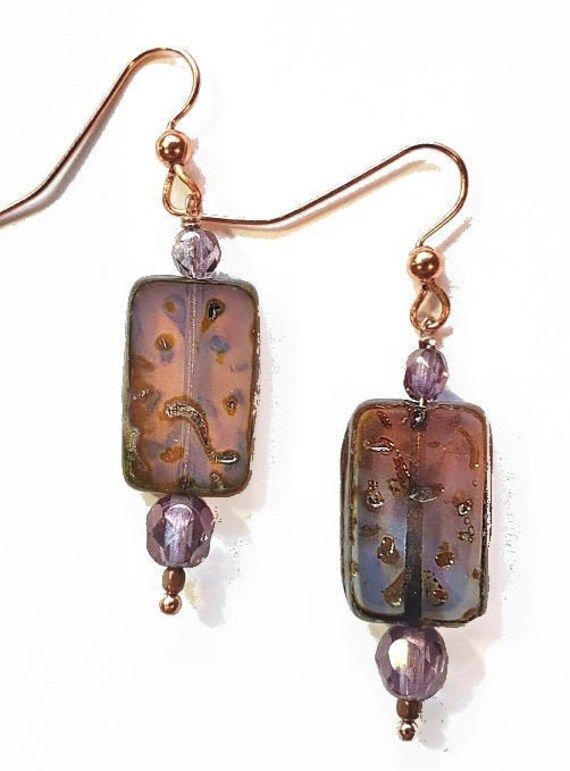 Purple, orange, and blue tones swirl in glass rectangles in these striking earrings. They are further enhanced with faceted purple beads and hang fro copper toned earwires. Length from ear wire is 1 inch. Rectangular Copper Earrings With Ear Wire, Rectangular Earrings, Purple Beads, Rectangle Earrings, Earring Designs, Purple Orange, Blue Tones, Ear Wire, Designer Earrings