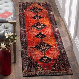 a long red rug on the floor next to a chair and vase with flowers in it