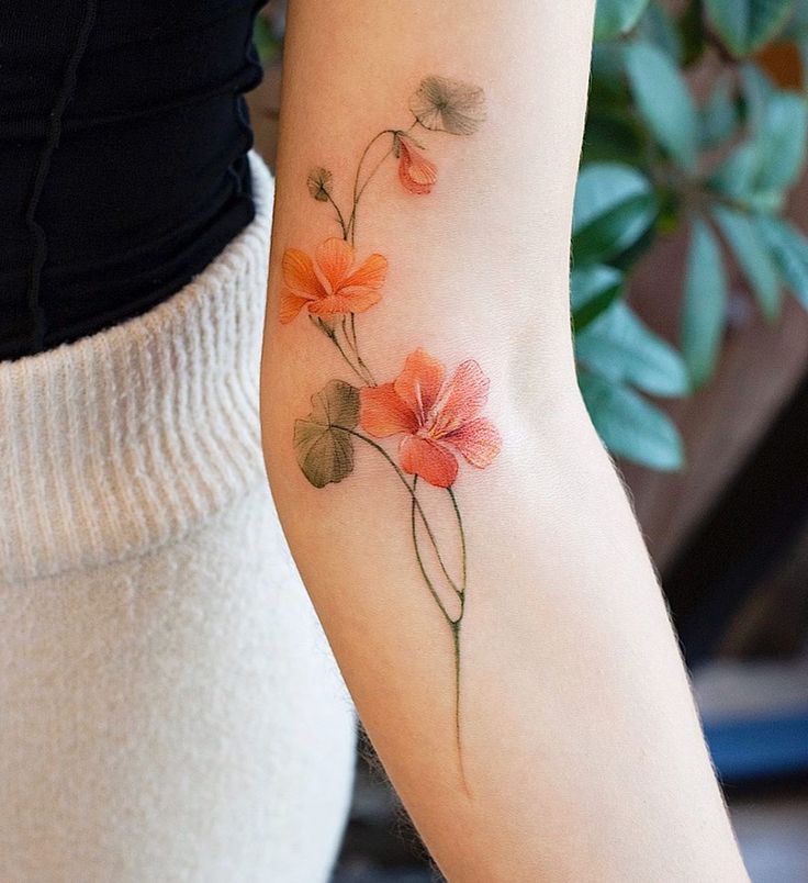 a woman's arm with an orange flower tattoo on the left side of her arm