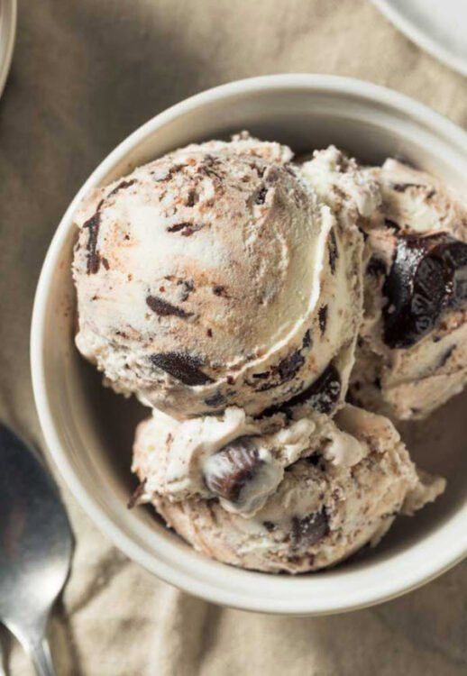 three scoops of ice cream in a white bowl on a table with spoons