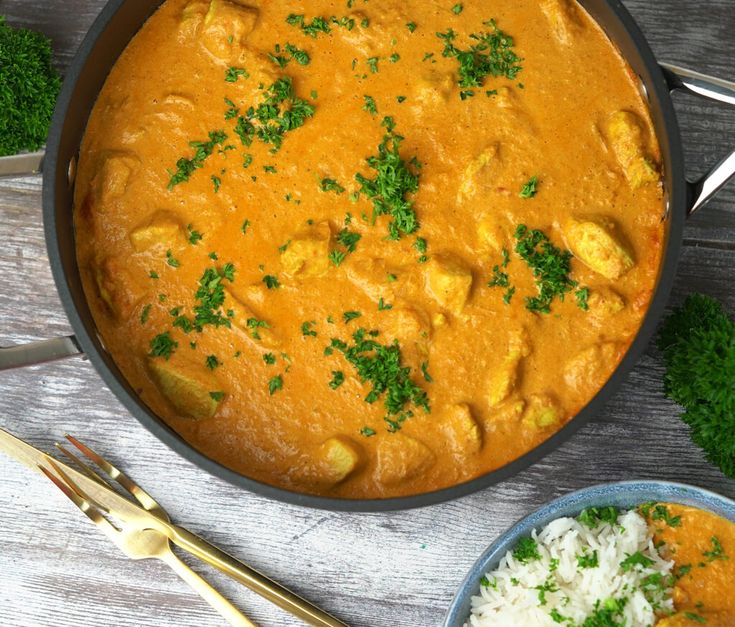 two bowls filled with curry and rice on top of a wooden table next to silverware