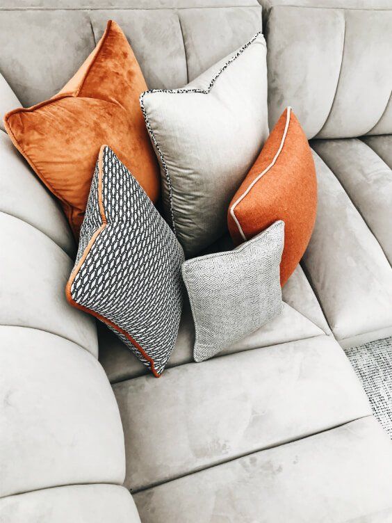 four different colored pillows sitting on top of a white couch with grey and orange accents