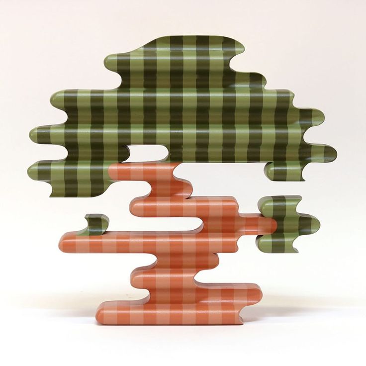 an abstract sculpture made out of green and orange plaid material with trees in the background