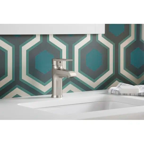 a bathroom sink with two faucets in front of a green and white wallpaper