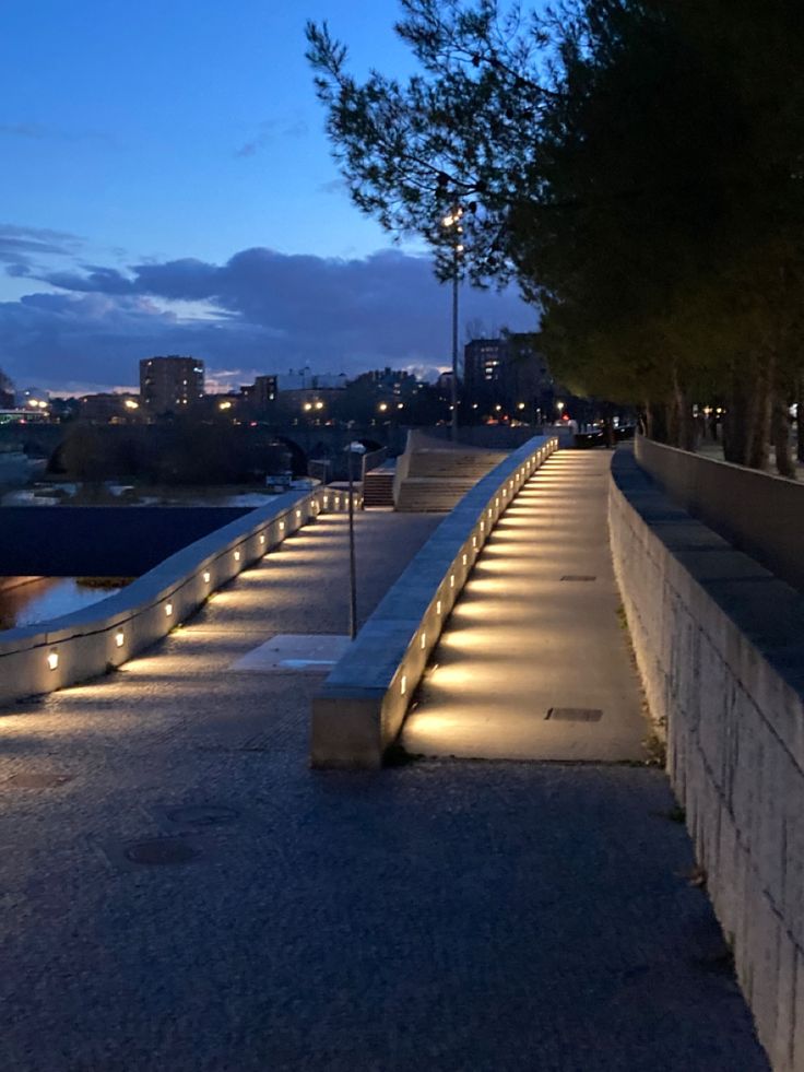 a row of concrete benches sitting on top of a sidewalk next to a river at night