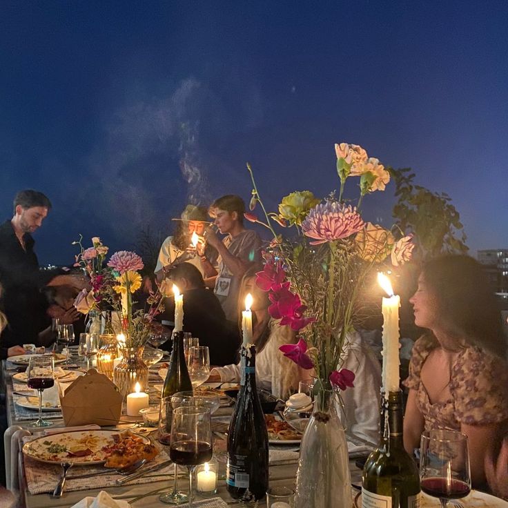 a group of people sitting around a table with food and drinks on it at night