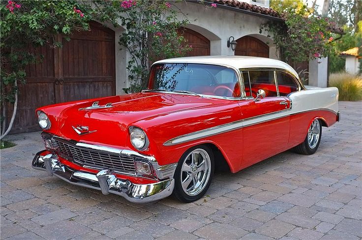 an old red and white car is parked in front of a house with a brick driveway