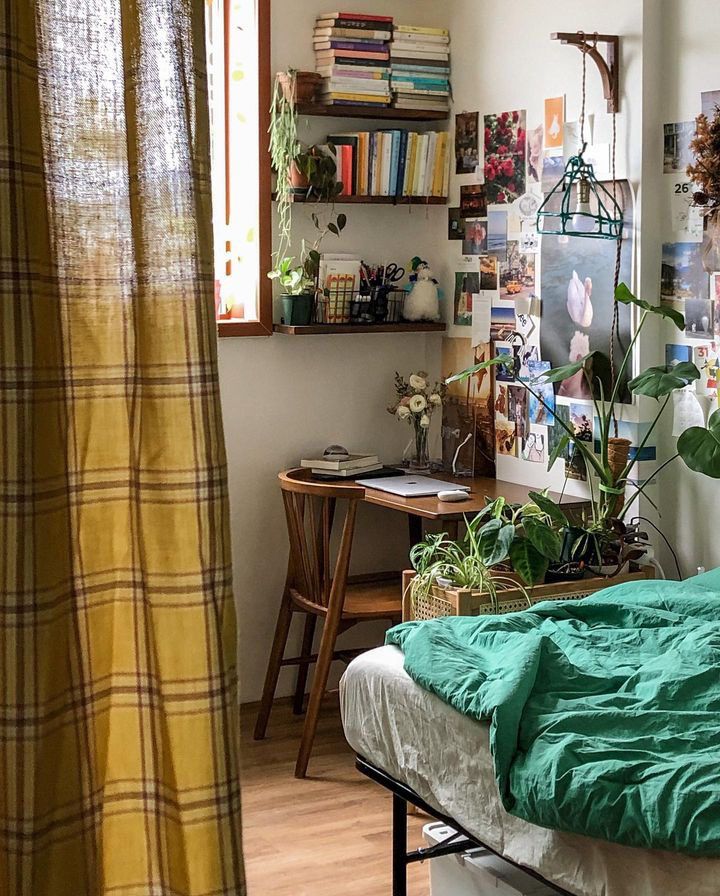 a bed sitting in a bedroom next to a window filled with green plants and books