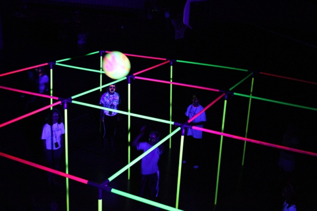 several people standing in an illuminated room with neon colored lines on the floor and one person holding a white ball