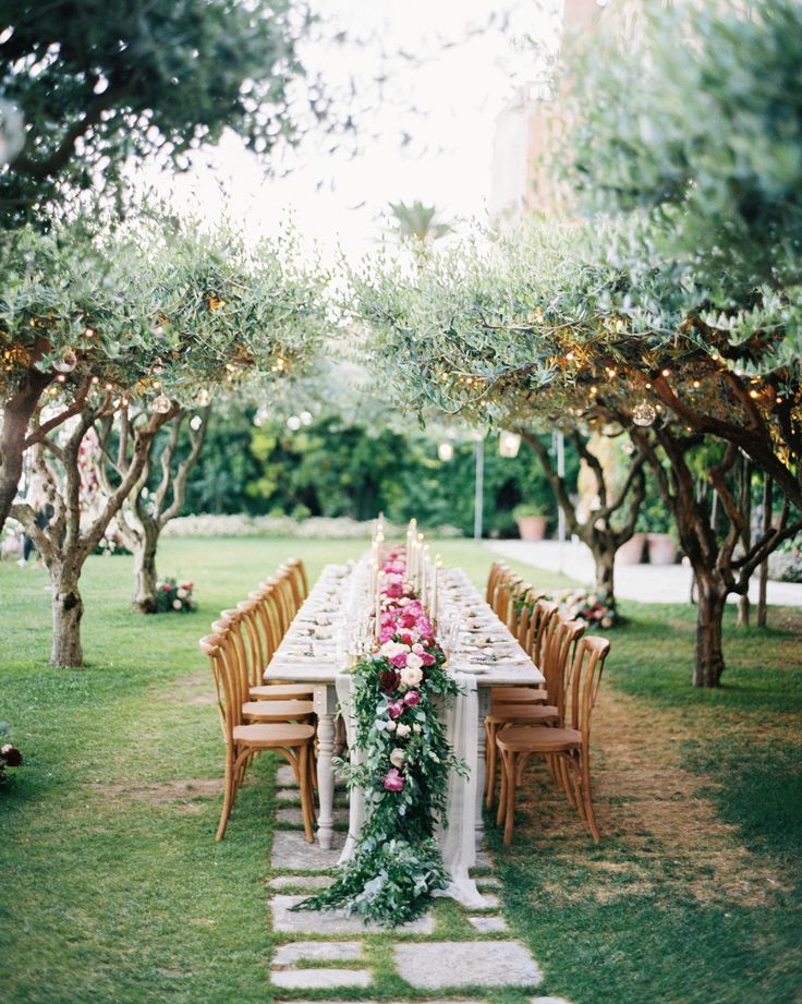 a long table set up with flowers and greenery for an outdoor dinner in the garden