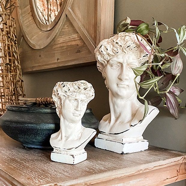 two white busturines sitting on top of a table next to a potted plant