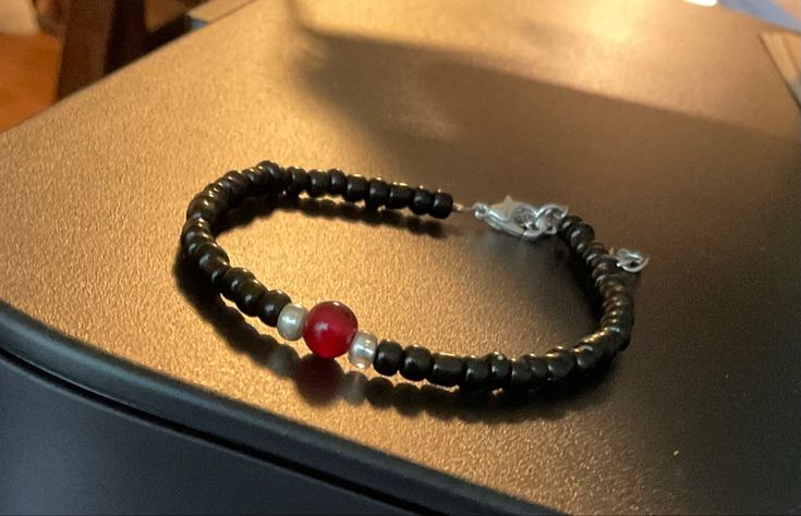 a black beaded bracelet with red and white beads sits on top of a table