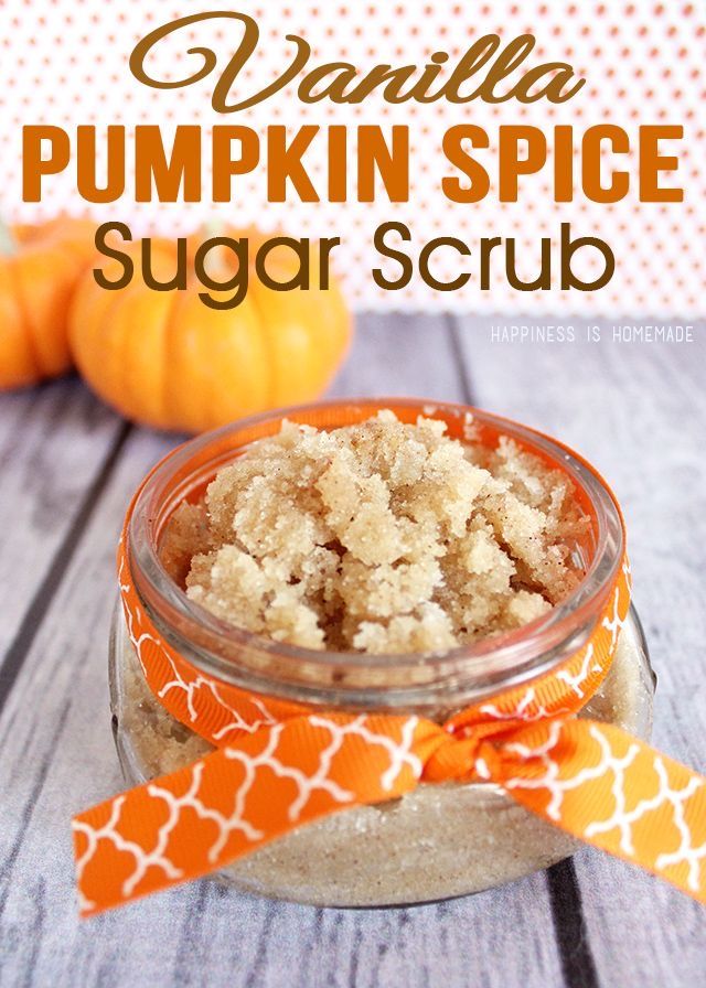 pumpkin spice sugar scrub in a glass jar on a wooden table with two small pumpkins behind it