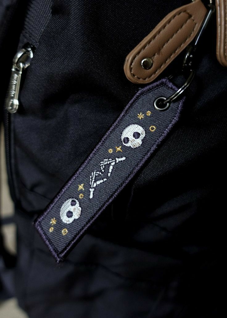 there is a skull and crossbones on the back of a bag strap that has a leather keychain attached to it