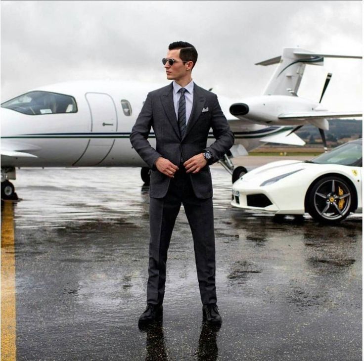 a man in a suit and tie standing next to a white sports car on the tarmac