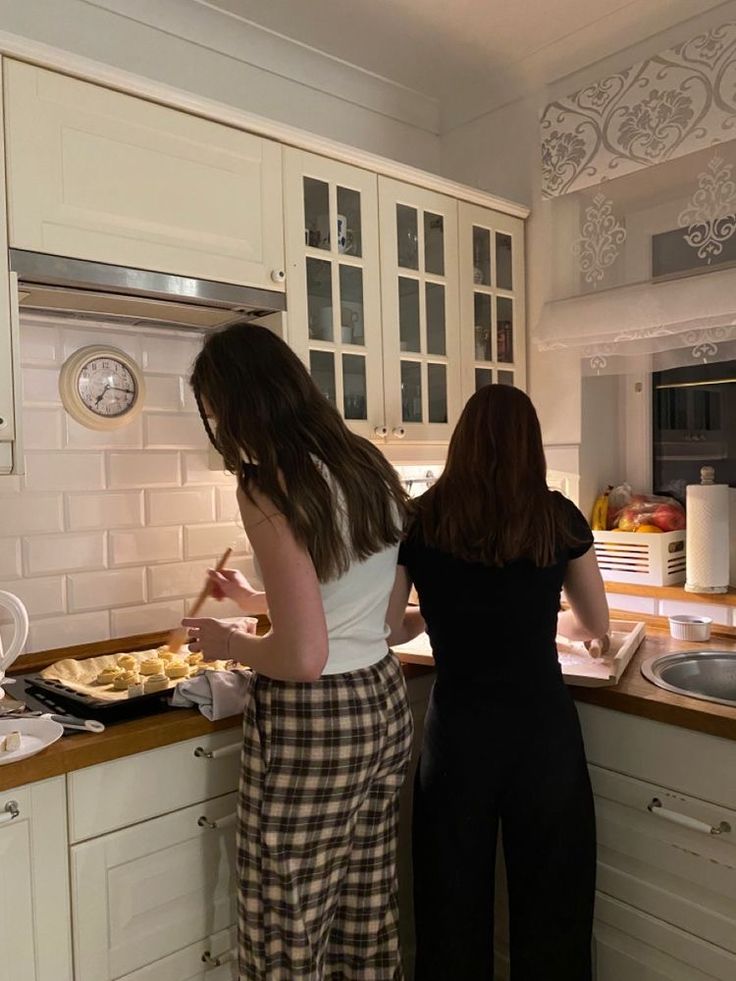 two women standing in a kitchen preparing food on top of a counter next to each other