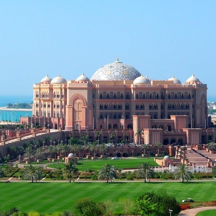 a large building sitting on top of a lush green field next to the ocean and palm trees