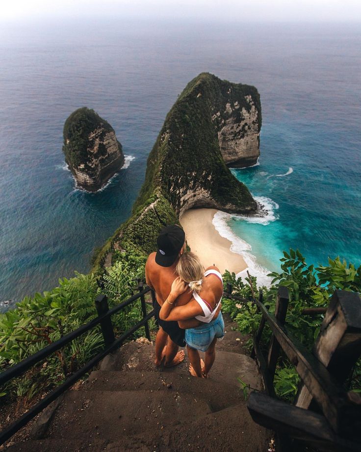 two people standing on the stairs looking at the ocean and cliffs in the distance,