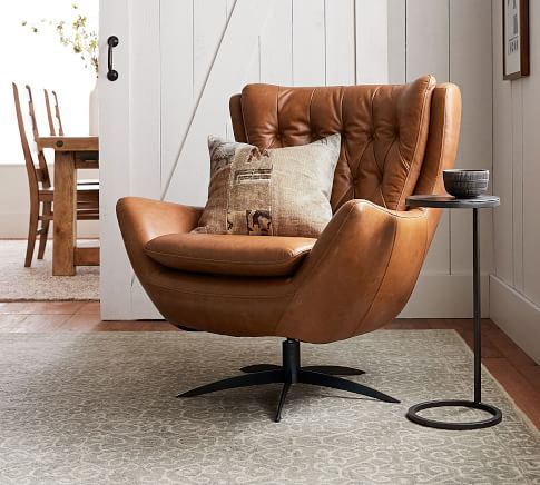 a brown chair sitting on top of a wooden floor next to a table with a pillow