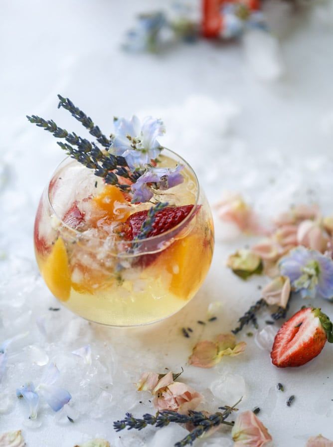 a glass filled with ice and fruit on top of a white table covered in flowers