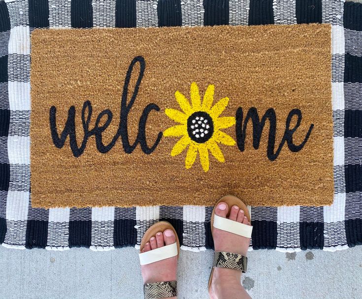 a person standing in front of a welcome mat that says welcome with a sunflower on it