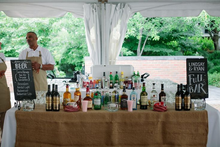 two men standing next to a table full of liquor bottles