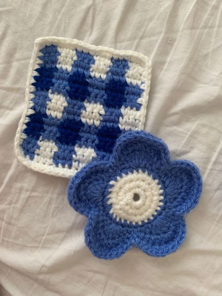 two crocheted blue and white flower coasters on top of a bed next to each other