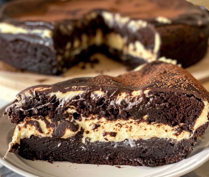 a piece of chocolate cake on a plate with the rest of the cake in the background