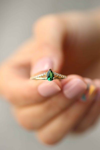 a woman's hand holding an emerald ring